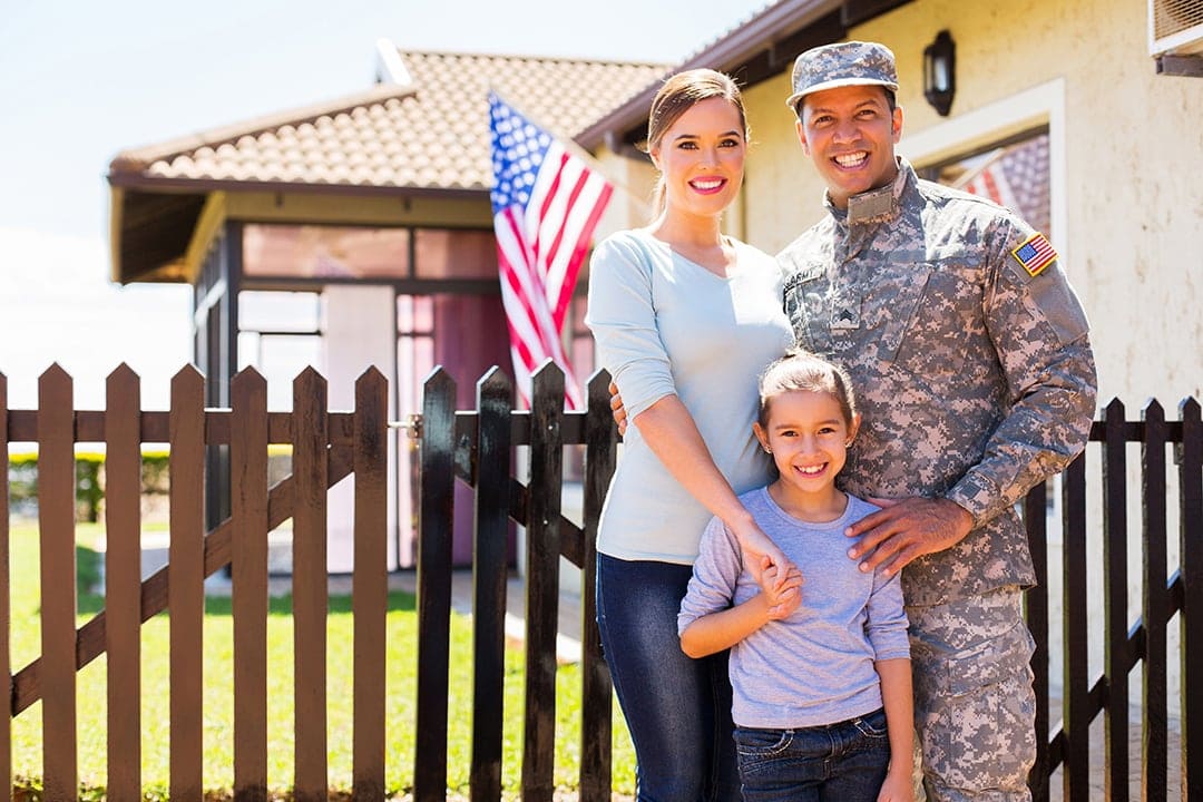 A smiling veteran and his family in front of their new home